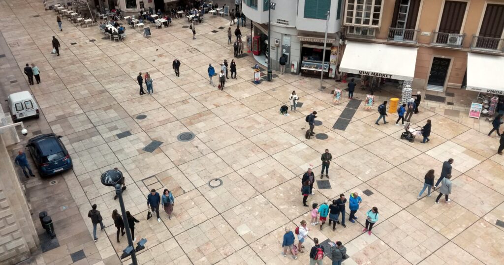 Busy town square seen from above, with people walking past small shops